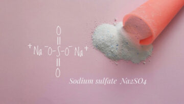 A pink scoop spills fine white powder—sodium sulfate (Na₂SO₄)—onto a soft pink surface, with its chemical structure elegantly illustrated beside it. The scene evokes cleanliness and precision, representing the high standards of Park Avenue Laundry, Bemidji, Minnesota 56601, where science meets spotless service.