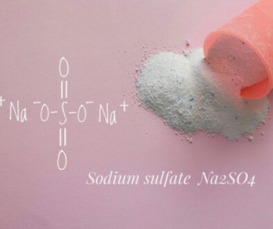 A pink scoop spills fine white powder—sodium sulfate (Na₂SO₄)—onto a soft pink surface, with its chemical structure elegantly illustrated beside it. The scene evokes cleanliness and precision, representing the high standards of Park Avenue Laundry, Bemidji, Minnesota 56601, where science meets spotless service.