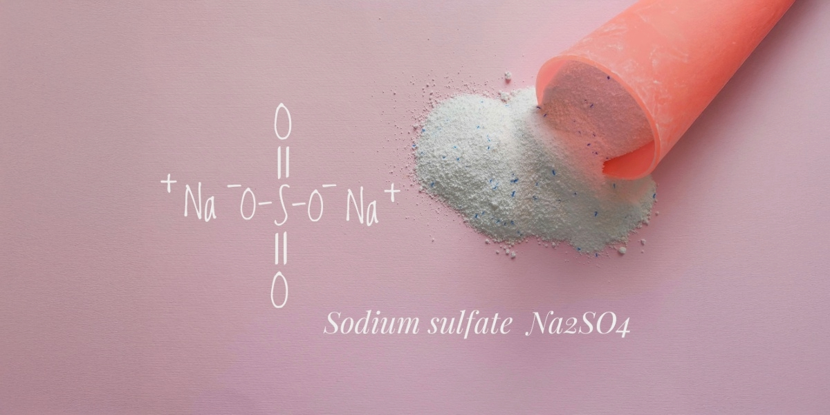 A pink scoop spills fine white powder—sodium sulfate (Na₂SO₄)—onto a soft pink surface, with its chemical structure elegantly illustrated beside it. The scene evokes cleanliness and precision, representing the high standards of Park Avenue Laundry, Bemidji, Minnesota 56601, where science meets spotless service.